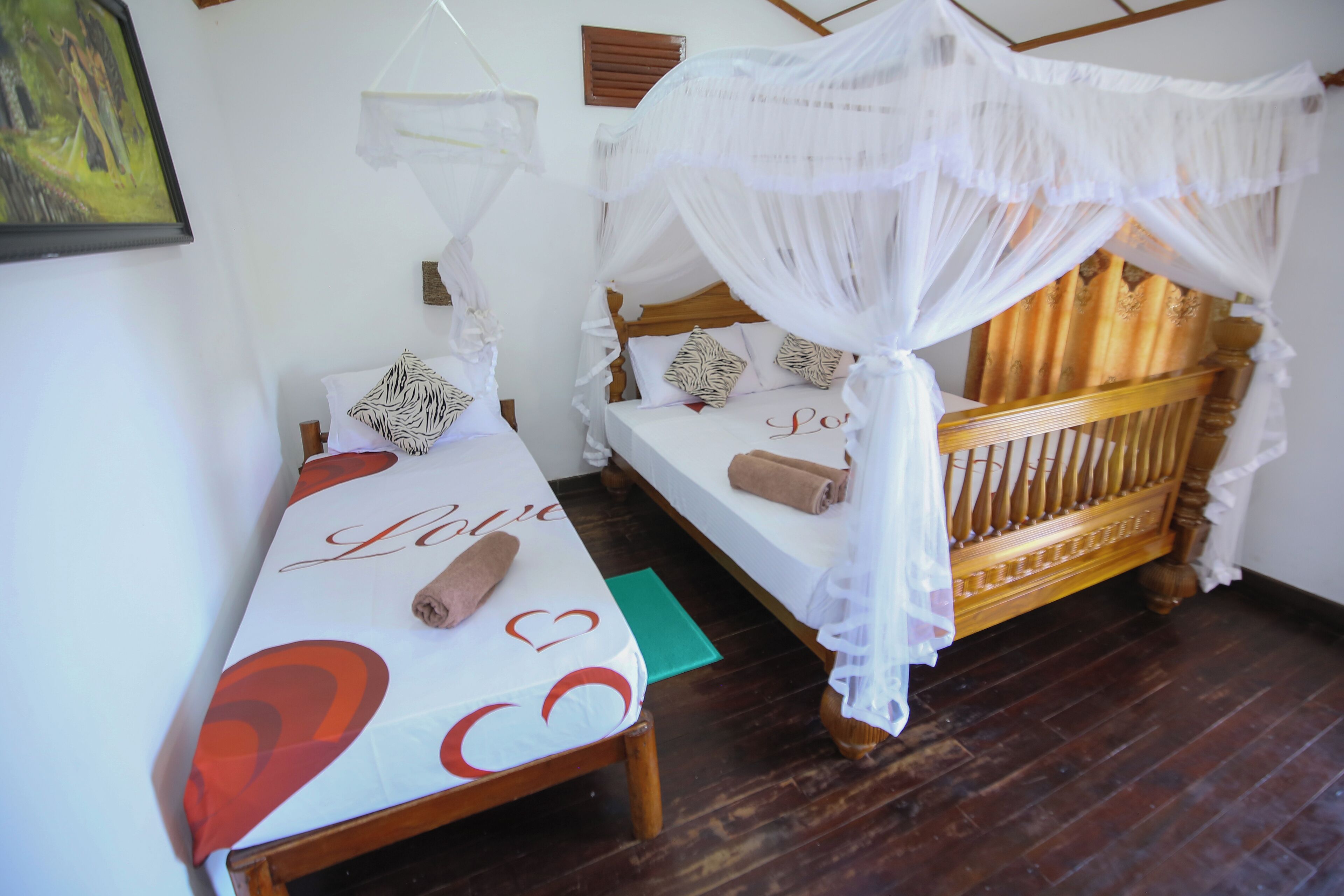 Una habitación con dos camas, una con dosel y la otra sin él. Cada cama tiene una almohada y una toalla enrollada.