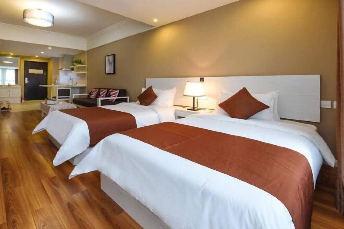 Habitación de hotel con dos camas, un escritorio, una silla y una lámpara.