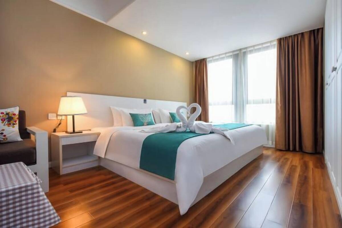 Habitación de hotel con cama, mesita de noche, lámpara y vistas al exterior.
