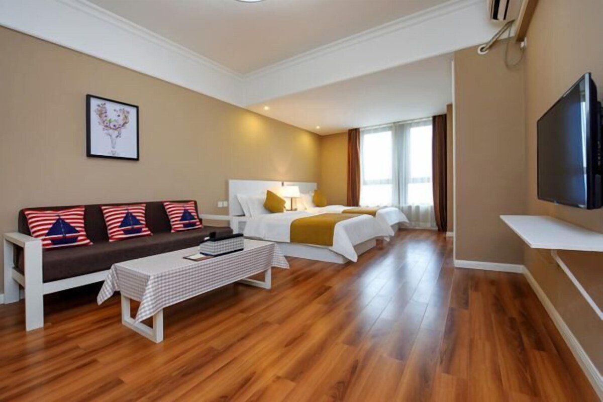 A hotel room with a sofa, two beds, a TV, and a painting on the wall.
