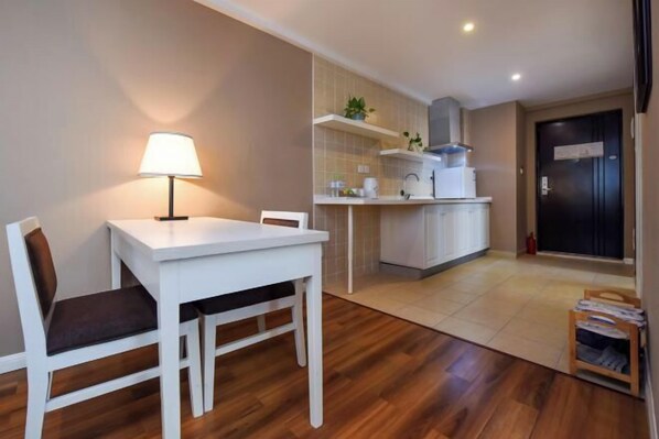 A compact kitchen with white cabinets, a small dining table with chairs, a lamp, and a tiled backsplash. - Sweetome Vacation Apartment (Galaxy) (Chongqing)