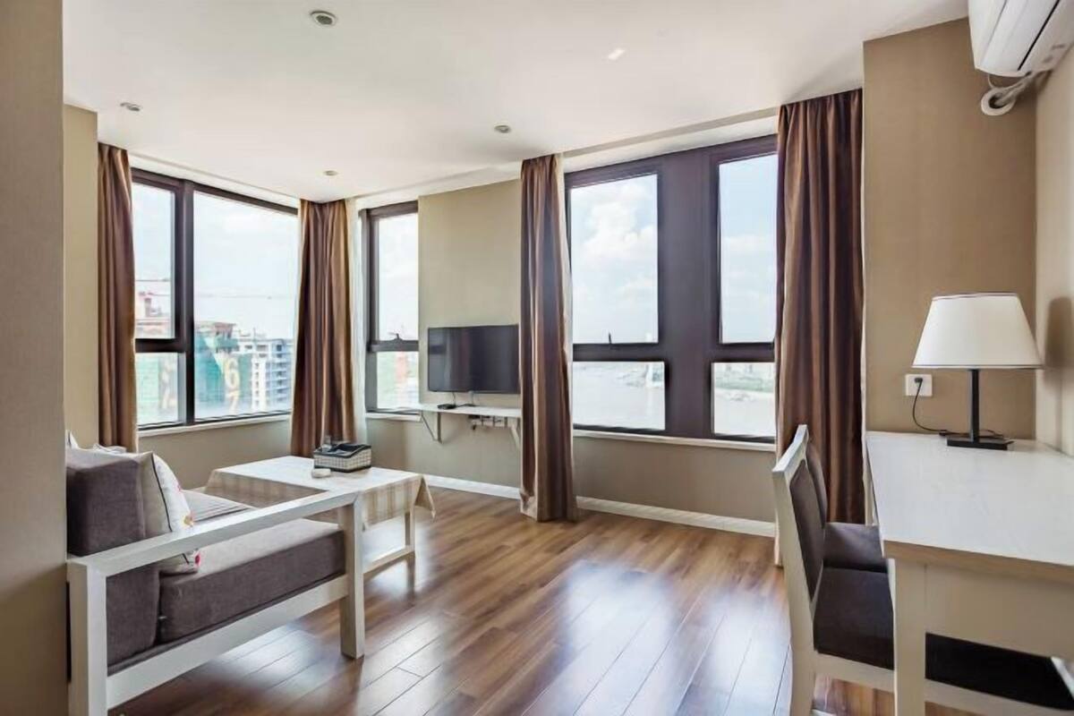 Una habitación de hotel moderna con sofá, escritorio, televisor y ventanas amplias.