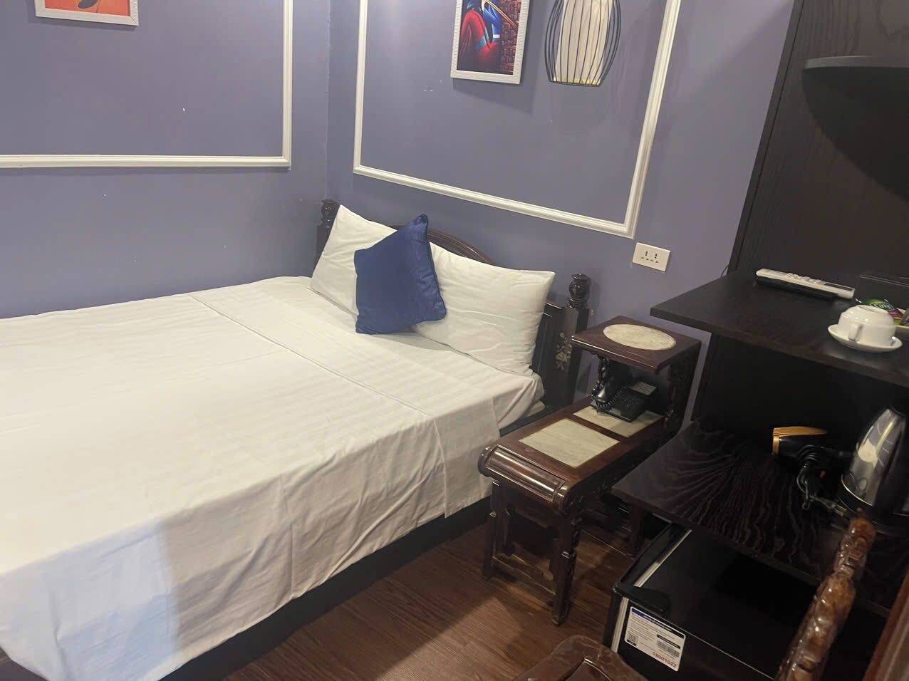 A hotel room with a bed, a small bedside table with a lamp, a chair, and a desk with a computer and a coffee maker.