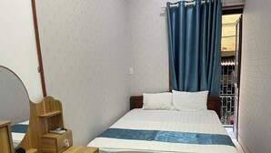 A bedroom with a wooden bed, a bedside table with a mirror, and a window with blue curtains. - Asia Cozy House (Hanoi)