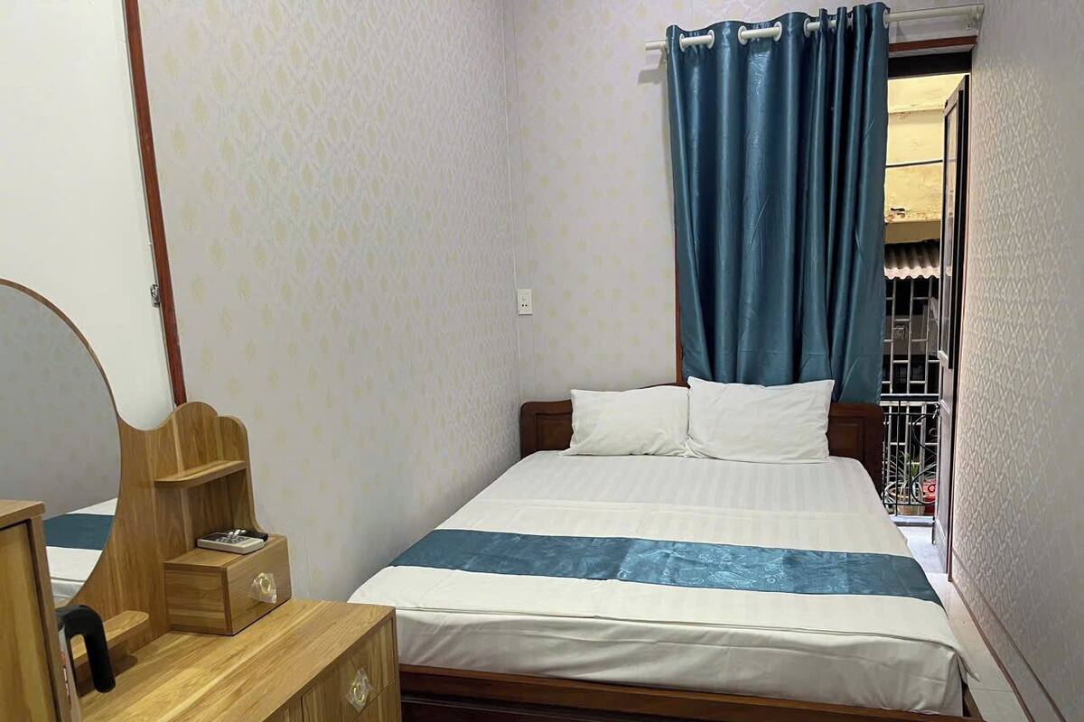 Un dormitorio con una cama de madera, una mesita de noche con espejo y una ventana con cortinas azules.