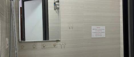 A bathroom with a shower, sink, and mirror. There is a sign on the wall with instructions.