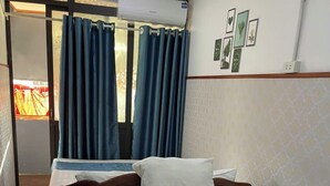 A hotel room with a bed, a wooden bench, and a window with blue curtains. - Asia Cozy House (Hanoi)