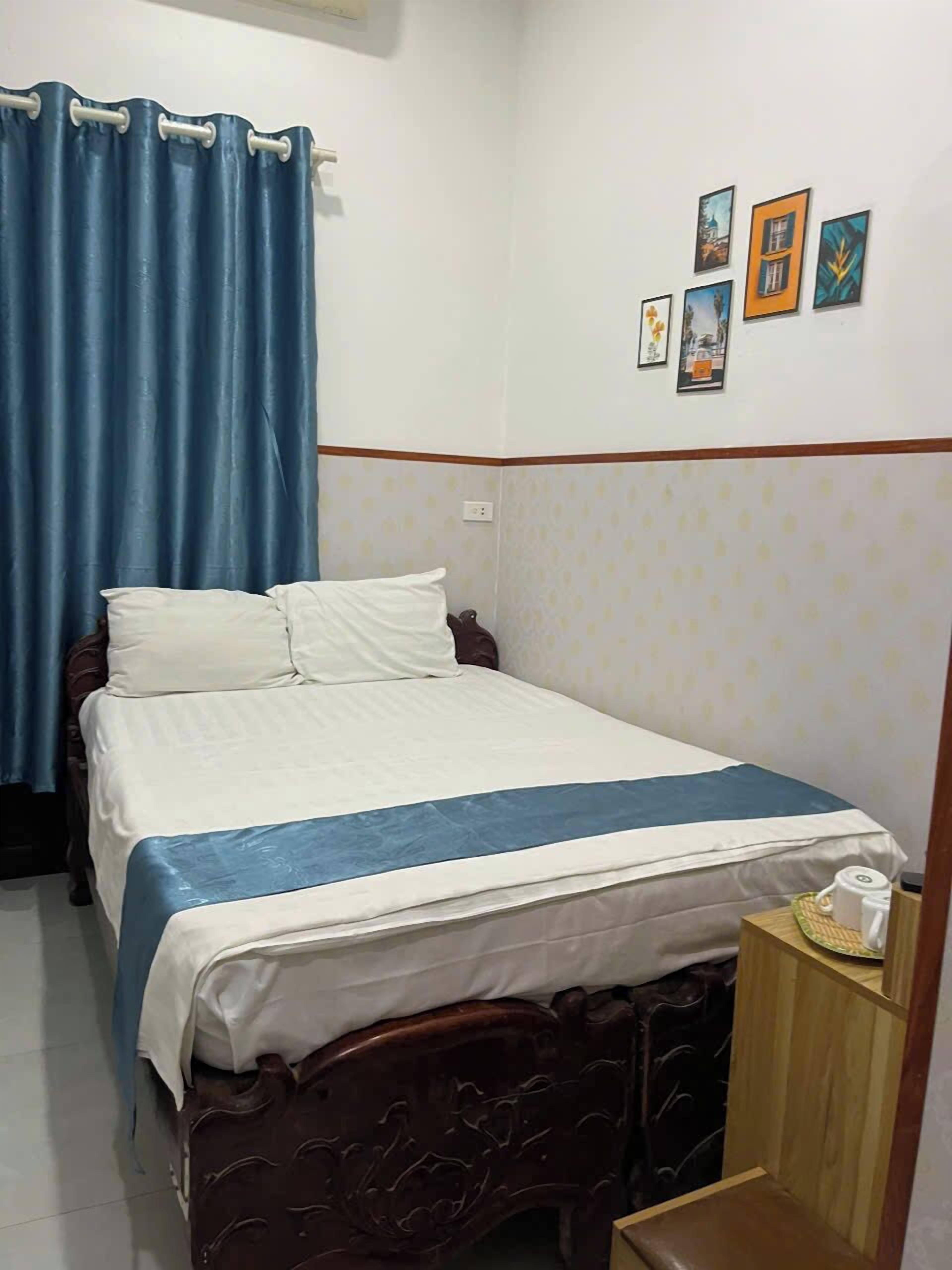 A bedroom with a bed, a wooden headboard, a nightstand, and a wall with framed pictures.