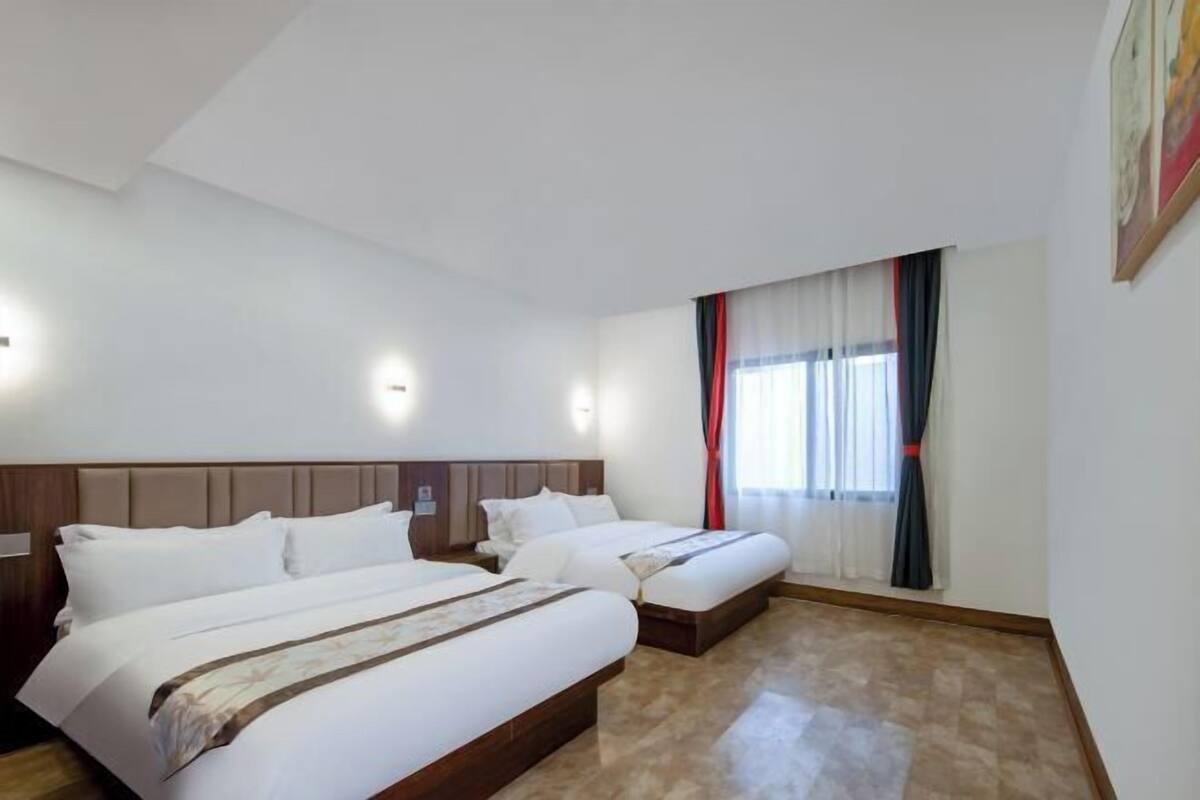 Una habitación de hotel con dos camas, un ventanal con cortinas y un cuadro en la pared.