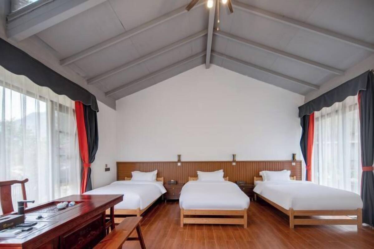 Habitación de hotel con dos camas, un escritorio de madera y un ventanal con cortinas.