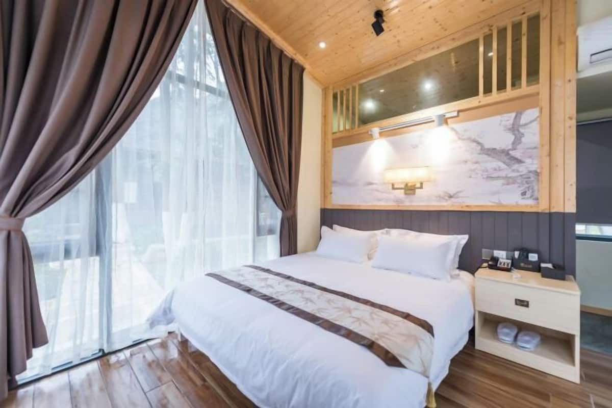 Una habitación de hotel con una cama grande, una mesita de noche, una lámpara y una ventana con cortinas.