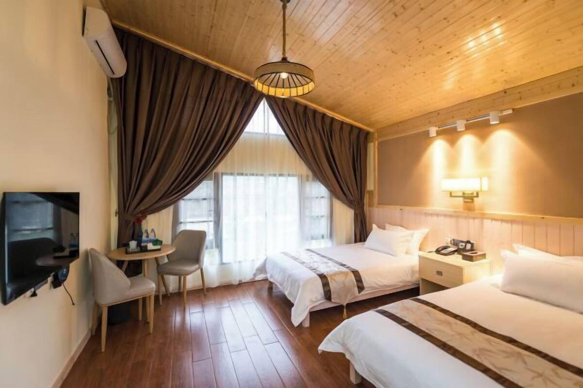 Habitación de hotel con dos camas, un escritorio con silla, televisión y un ventanal con cortinas.
