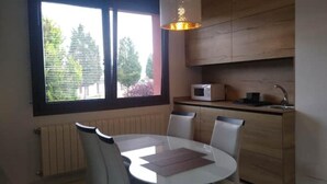 A compact kitchen with a dining area, a window with blinds, a microwave, and a hanging light fixture.
