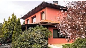 A two-story house with a red exterior, surrounded by greenery and flowering trees.