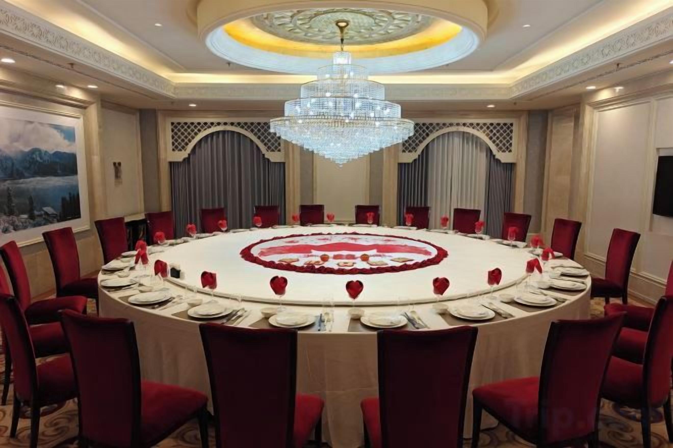 Une salle de conférence avec une table ronde, des chaises rouges et un lustre.
