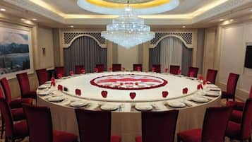 Un salón de conferencias con una mesa redonda, sillas rojas y un candelabro.