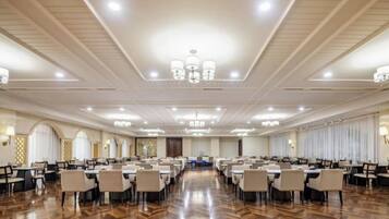 Un amplio salón de banquetes con filas de mesas y sillas, techos altos con candelabros y un piso de madera pulida.