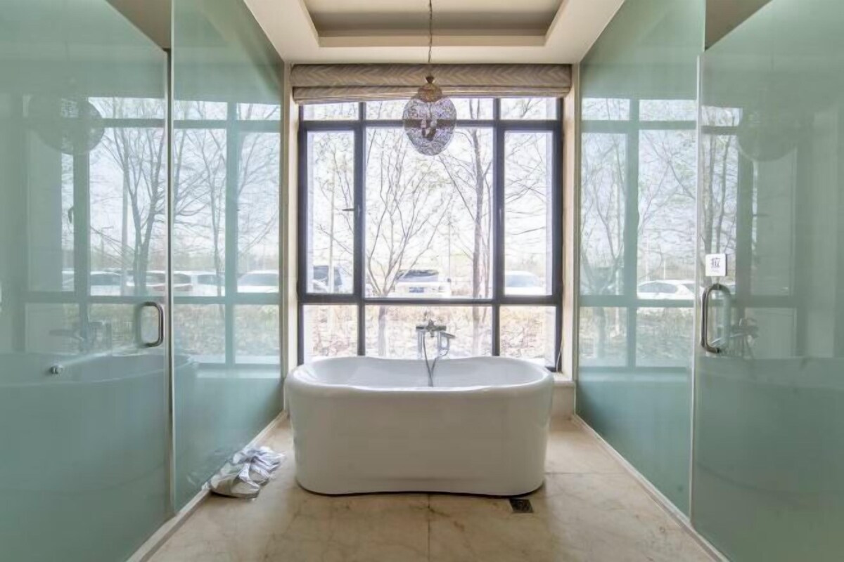 Ein modernes Badezimmer mit freistehender Badewanne, großen Fenstern und Duschabtüren aus Glas.