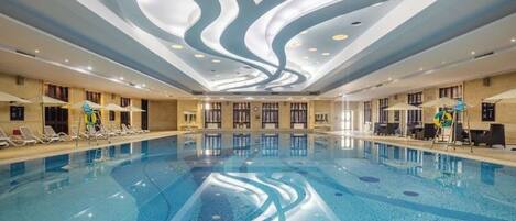 Una piscina interior con un diseño moderno de techo, sillas de descanso y una vista despejada del área de la piscina.