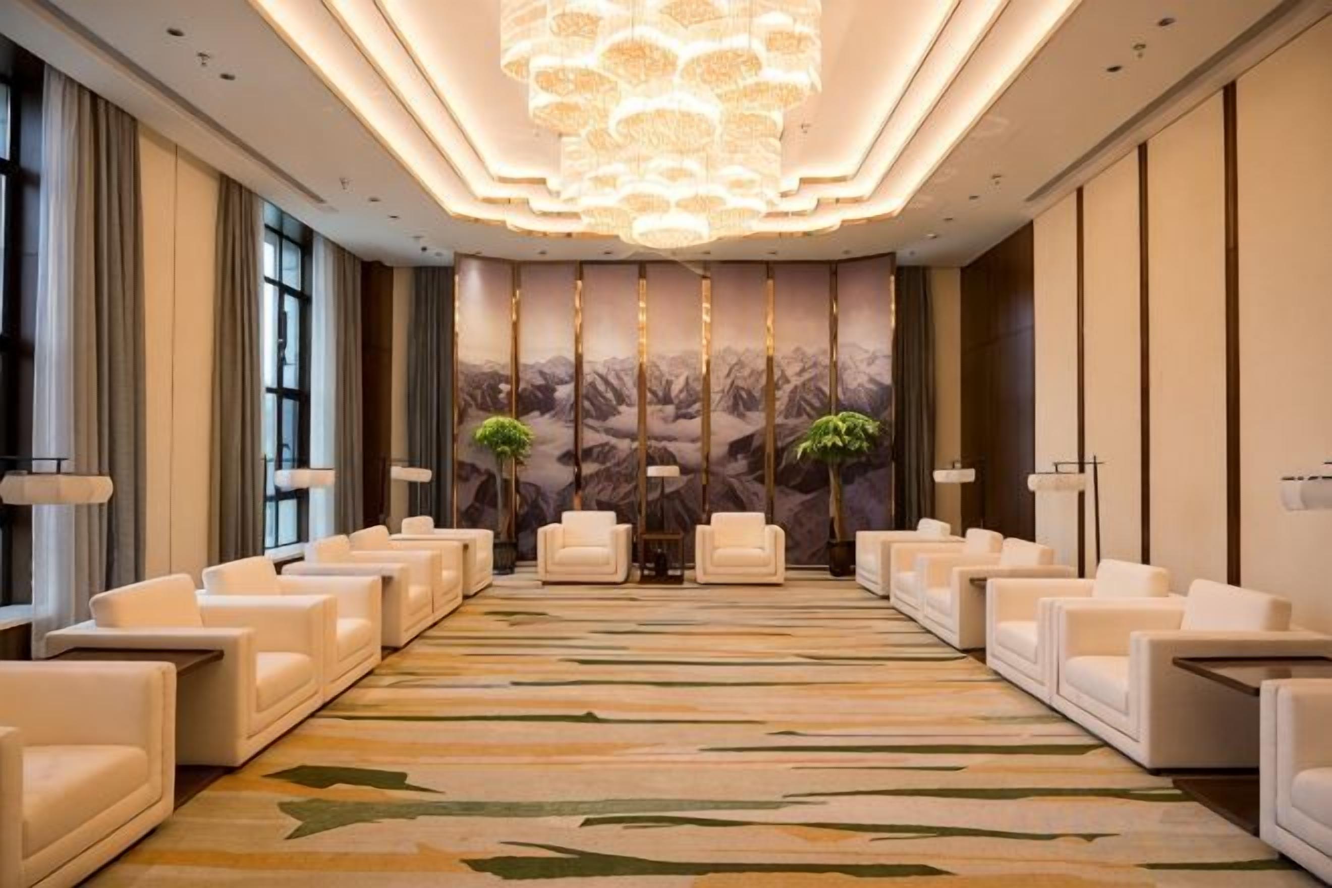 Un hall d’hôtel avec une longue rangée de canapés blancs, une moquette à motifs et un grand lustre.