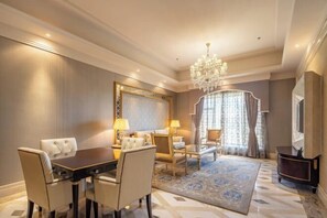 Quarto de hotel com área de refeições, um lustre, um espelho grande e uma televisão.