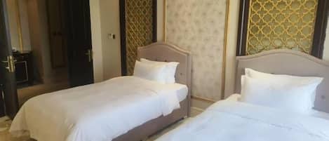 A hotel room with two beds, a chandelier, and patterned walls.