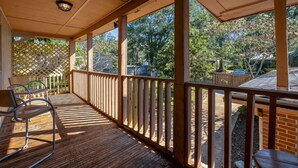 Eine überdachte Holzterrasse mit Geländer, einem Stuhl und einem Tisch.