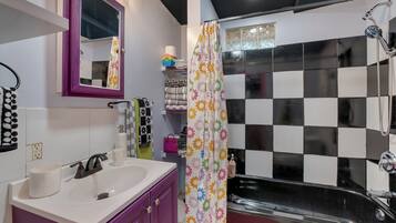 Ein Badezimmer mit einem weißen Waschbecken, violetten Schränken, einem Spiegel und einer Dusche mit schwarz-weiß karierter Wand sowie einem blumigen Duschvorhang.