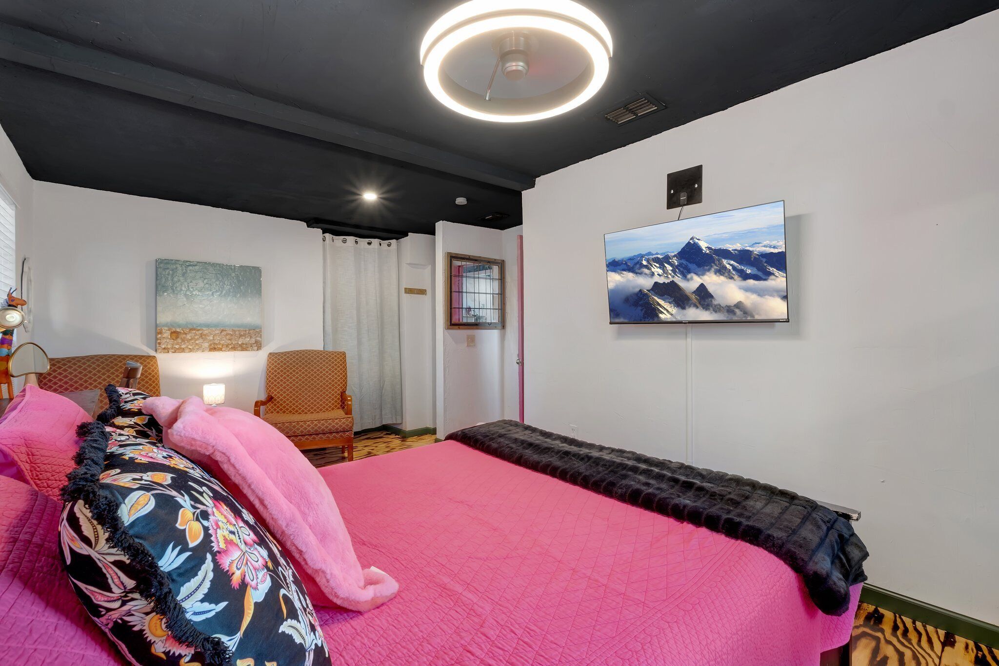 Un dormitorio con una cama grande, una silla, un cuadro y un televisor en la pared.