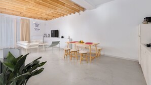 Un salon moderne avec un plafond en bois, un coin repas comprenant une table et des chaises, un canapé, un téléviseur et un radiateur.