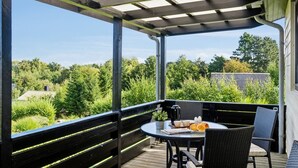 Un espace extérieur abrité, avec une table et des chaises, offrant une vue sur un paysage boisé.