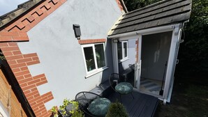 A small house with a brick exterior, a sliding glass door, a patio with a table and chairs, and a small garden area. - Coventry Cozy Cottage (Coventry)