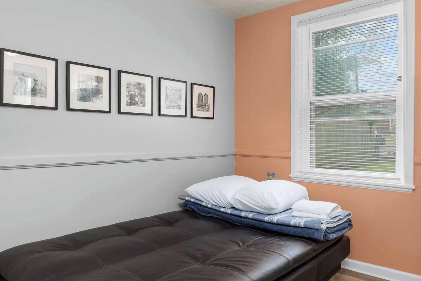 Une chambre à coucher avec un lit, une fenêtre avec des stores et quatre tableaux encadrés accrochés au mur.