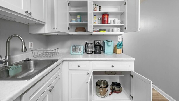 A compact kitchen with white cabinets, a stainless steel sink, a toaster, a coffee maker, and a spice rack.