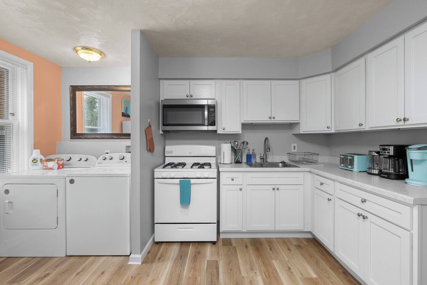 Une cuisine de taille réduite avec des meubles blancs, un four à micro-ondes, une cuisinière et un évier.