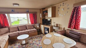 Un intérieur de camping-car accueillant, avec un canapé, une petite table, un téléviseur et une horloge au mur.