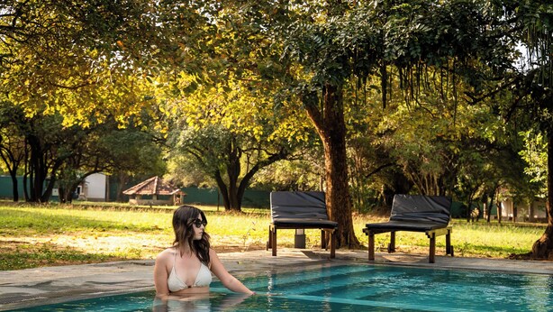 A woman in a swimming pool with two lounge chairs and trees in the background. - Pothana Village (Sigiriya)