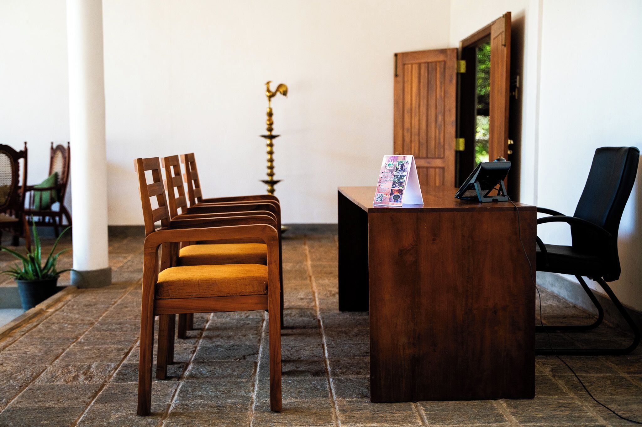A reception area with a wooden desk, a black office chair, and a wooden chair with a cushion.