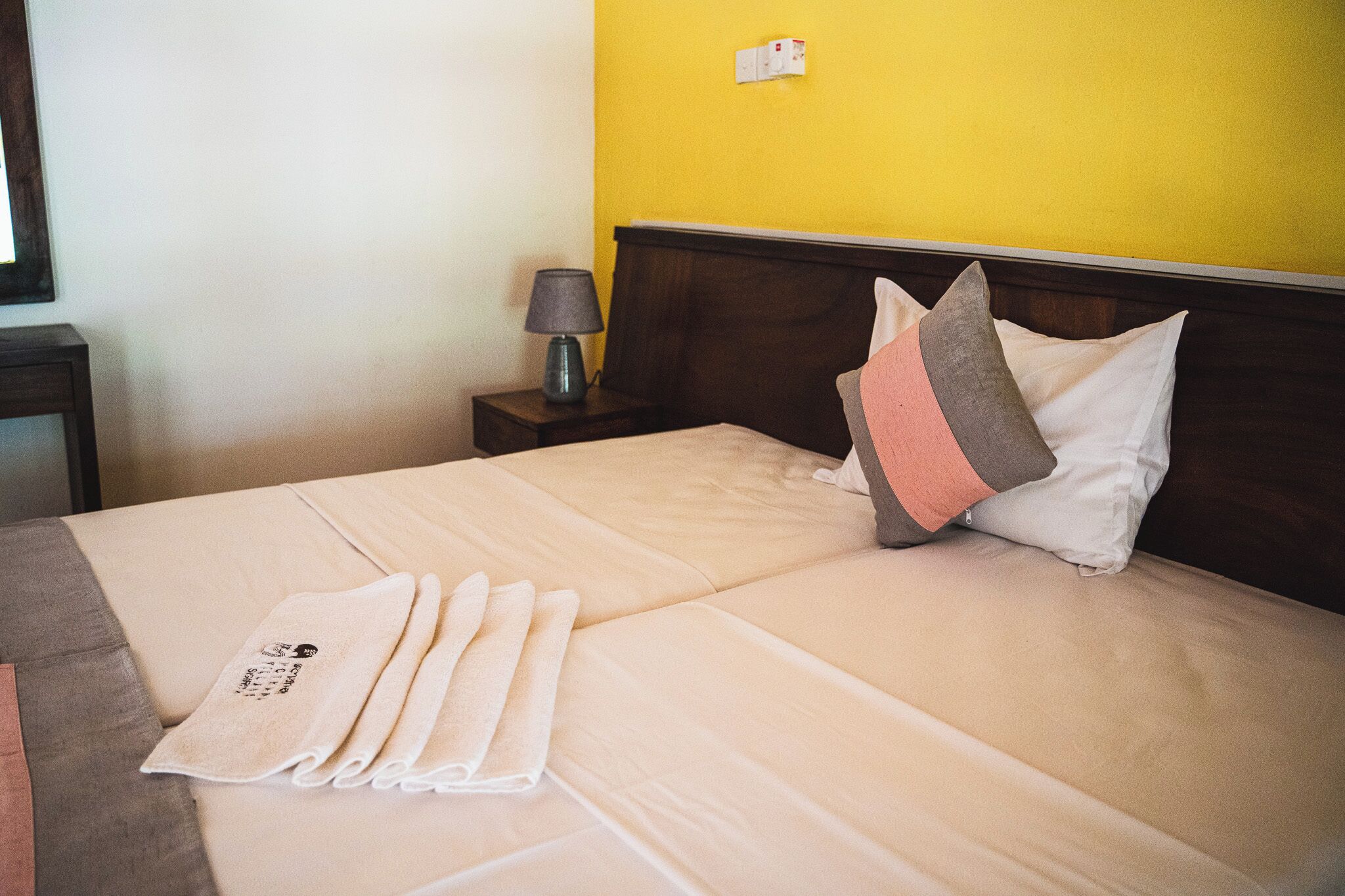 Un lit bien fait, avec une couverture beige, des oreillers et une serviette pliée.