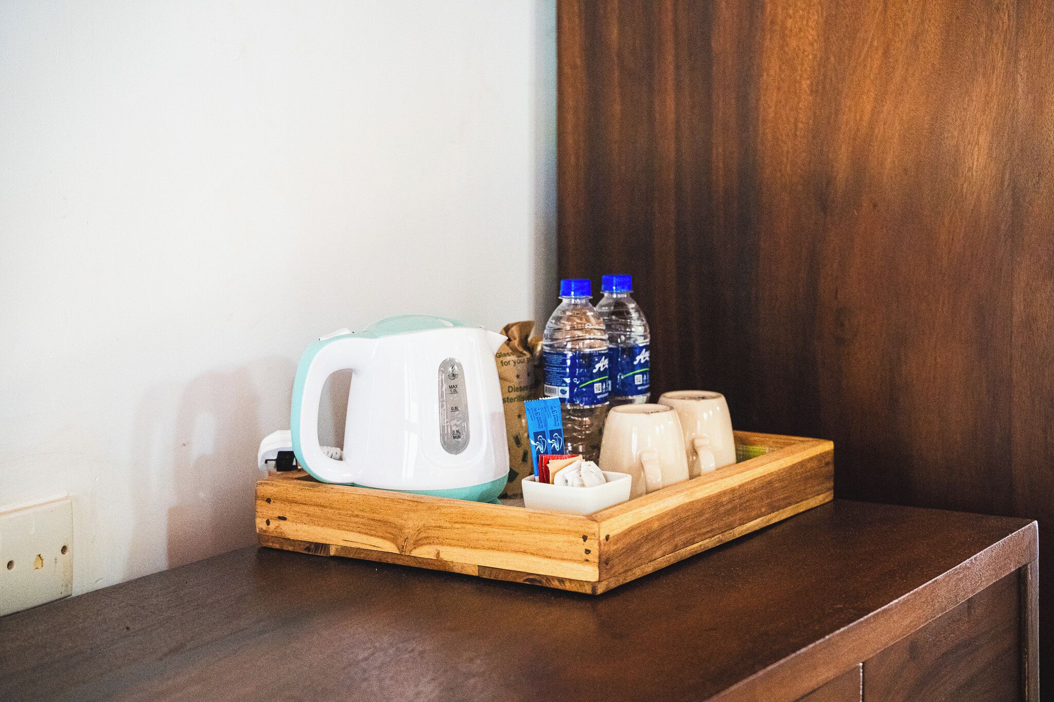 A wooden tray with a kettle, two water bottles, and some food items on a dark wooden surface.