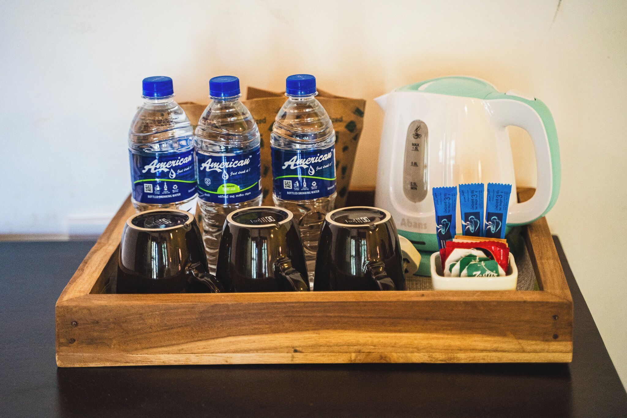 Una bandeja de madera con botellas de agua estadounidense, una taza blanca y sobres de té o café.