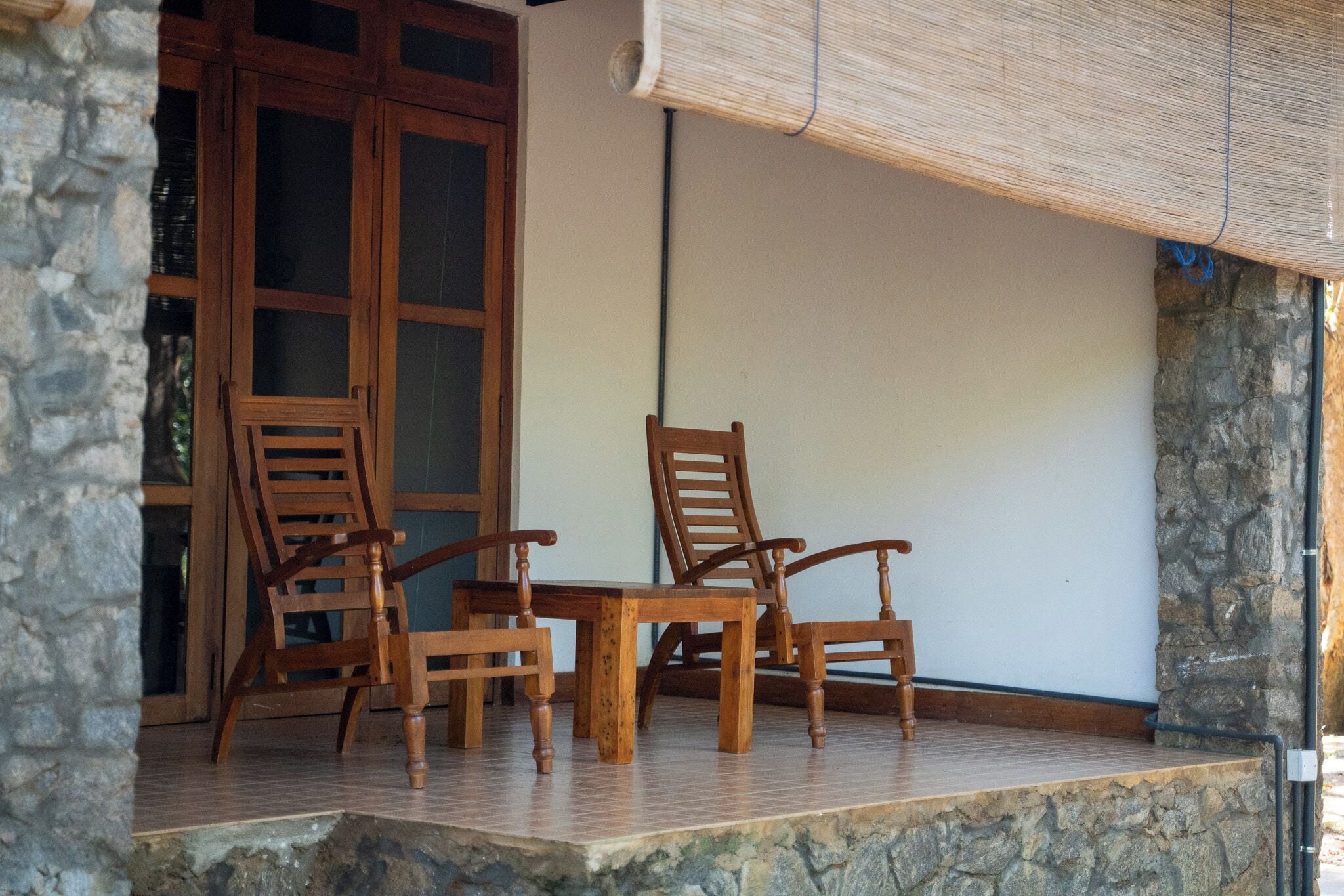 Un porche dallé de pierres, avec des chaises et une table en bois.
