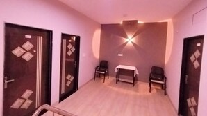 A hotel room with a wooden floor, two chairs, a small table, and a wall-mounted light fixture. - Hotel Global Inn (Indore)