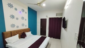 A bedroom with a bed, a ceiling fan, a wall-mounted TV, and a door. - Hotel Global Inn (Indore)