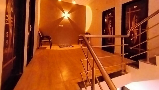 A hallway with a wooden floor, a chair, and a staircase with metal railings. - Hotel Global Inn (Indore)