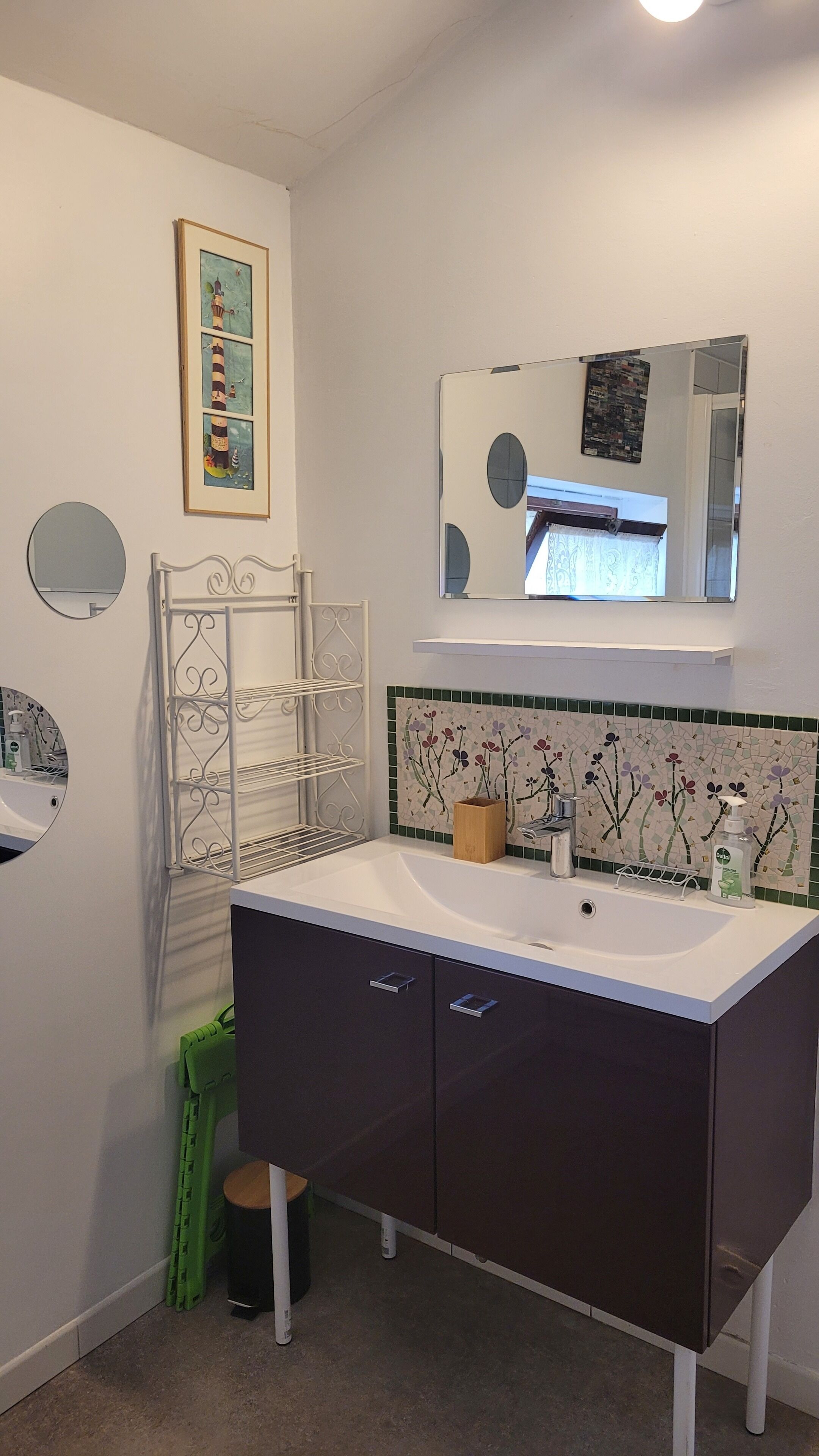 Un bagno con lavandino bianco, mobili scuri, uno specchio e un rivestimento in piastrelle decorativo.