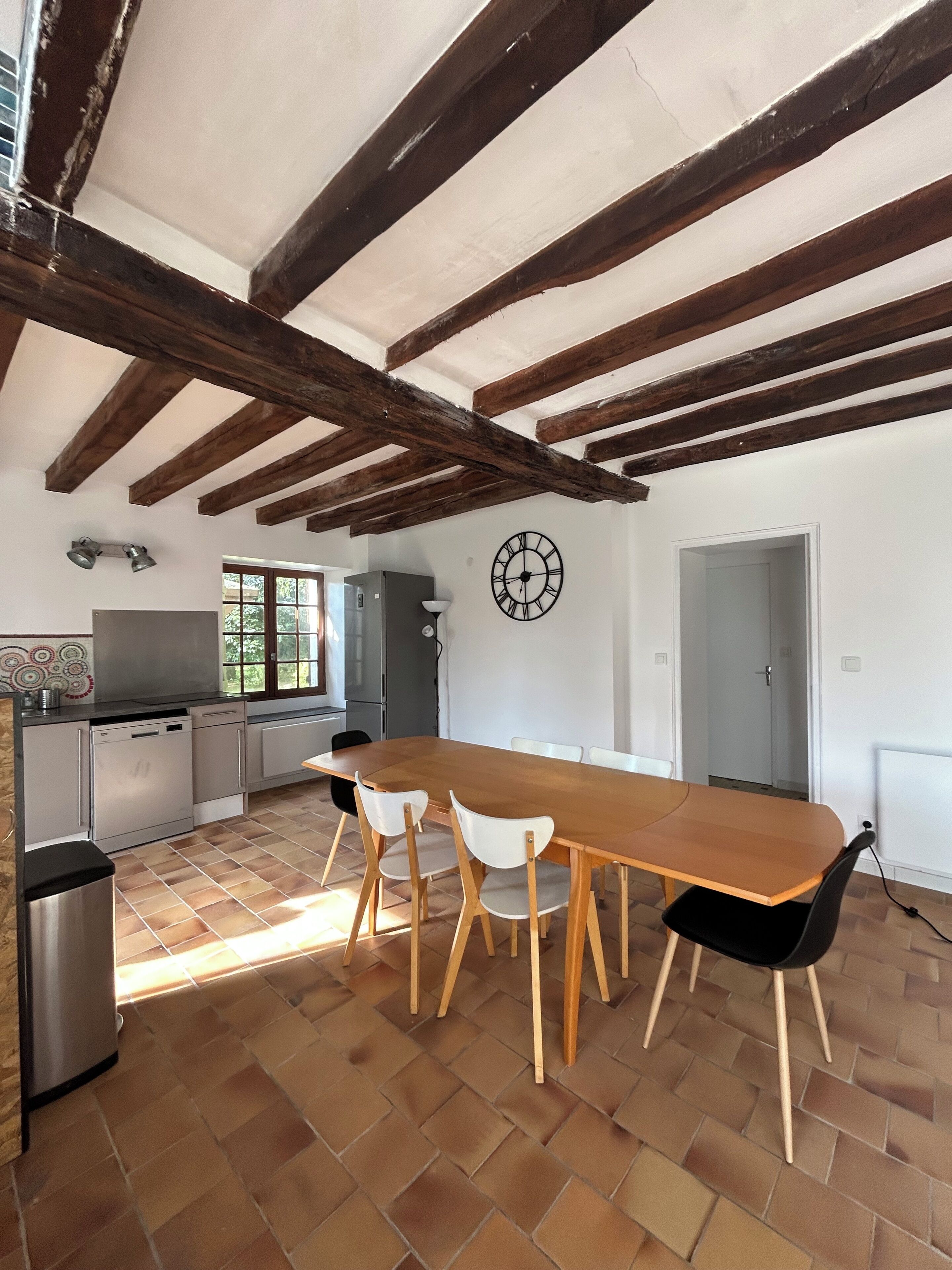 Una cocina amplia con una gran mesa de madera y sillas, un reloj en la pared y un ventanal que proporciona luz natural.