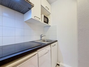 A compact kitchen with a black countertop, white cabinets, a stainless steel sink, and a Bosch dishwasher.
