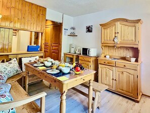 A cozy kitchen with wooden cabinets, a dining table set with plates, bowls, and a fruit bowl. There is a microwave and a coffee maker on the counter.