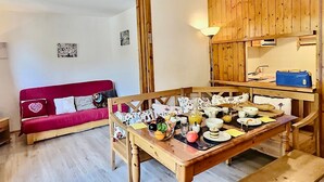 A cozy room with a wooden dining table set for breakfast, a red sofa with heart-patterned cushions, and a wooden cabinet above the table.